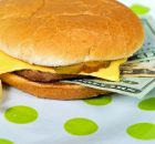A picture of a hamburger garnished with 20 dollar bills representing the high costs of food.